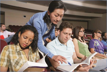 The photo shows a teacher reaches past a student to point to specific text.