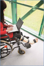 The  photo shows a female student in a wheelchair working on her laptop computer.