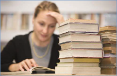 The photo shows a female student looking tired as she tries to focus on one of many books.