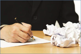 
The photo shows a  person writing with a pen, surrounded by crumpled paper from previous attempts.